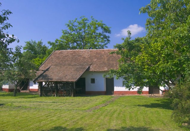 A képen a füzesgyarmati tájház hátsó traktusa látható, a hosszított tető alatt egy lőcsös kocsival.